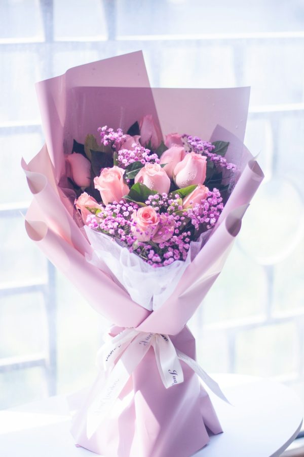 Pink roses with small purple flowers, wrapped in lilac and white paper.