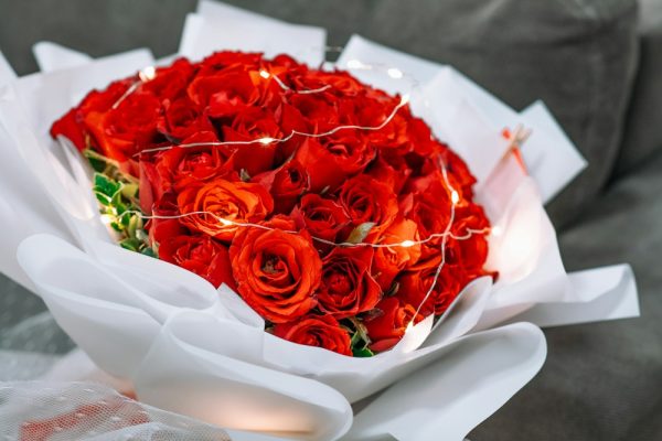 Red roses wrapped in light paper with a ribbon.